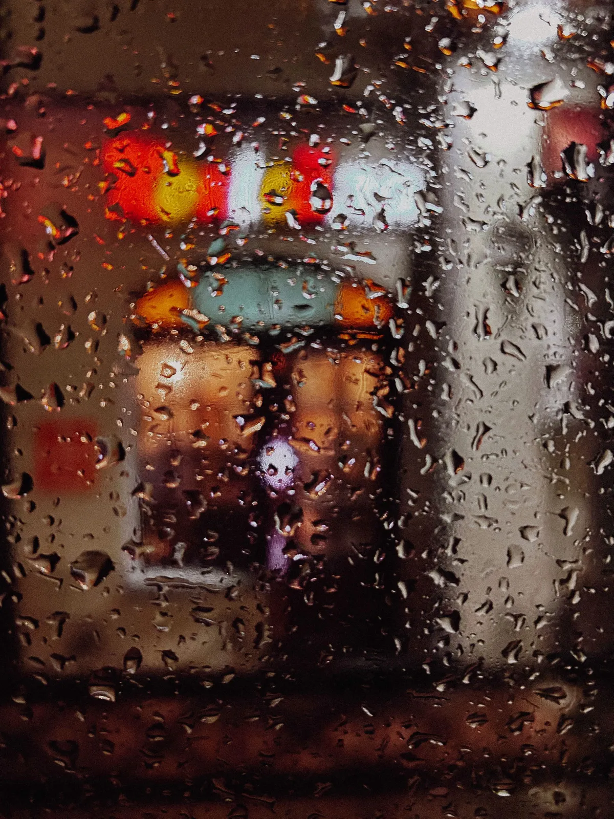 雨滴打在窗玻璃上，窗外辦公室燈光暈染模糊，氛圍低沉孤立